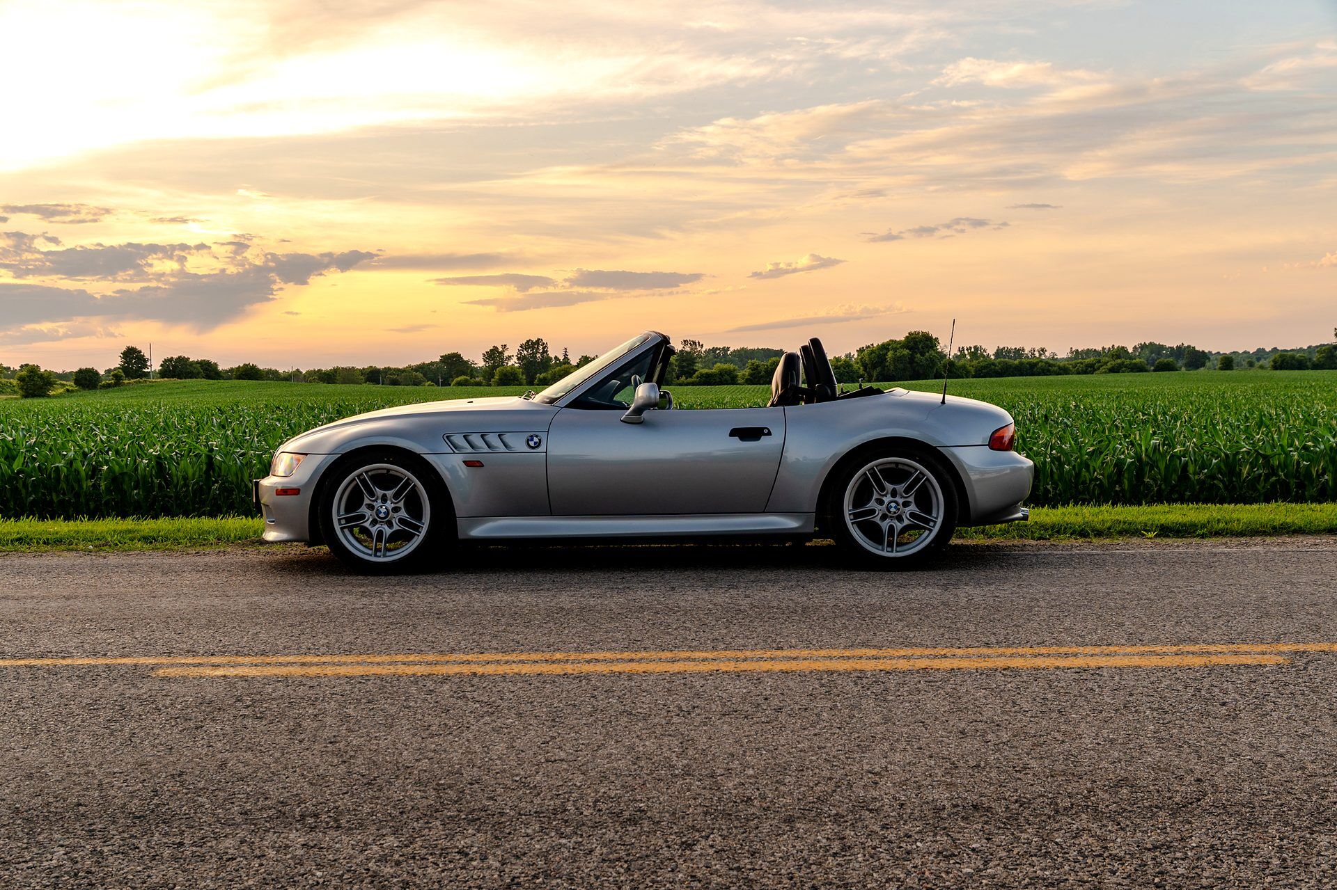 BMW Z3 side profile at sunset beside a cornfield